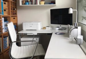Biuro z narożnym biurkiem, na którym stoi drukarka i ekran
